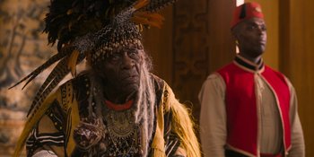 Movie still from “Coming 2 America” (2021), directed by Craig Brewer – An older man wearing a feather headdress; Close Up shot, Over the shoulder angle