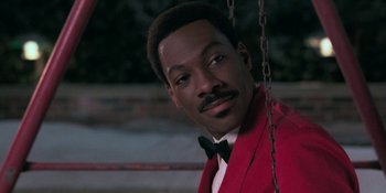 Movie still from “Coming 2 America” (2021), directed by Craig Brewer – A person wearing a suit and bow tie; Close Up shot, Over the shoulder angle