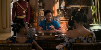 Movie still from “Coming 2 America” (2021), directed by Craig Brewer – A man sitting at a table in front of other people; Medium shot, Over the shoulder angle