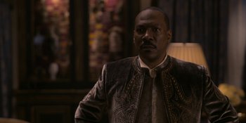 Movie still from “Coming 2 America” (2021), directed by Craig Brewer – A man wearing a suit and tie standing in front of a wall; Close Up shot, Over the shoulder angle