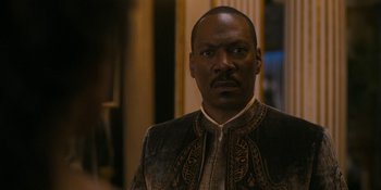 Movie still from “Coming 2 America” (2021), directed by Craig Brewer – A man in a suit and tie standing in front of a building; Close Up shot, Over the shoulder angle