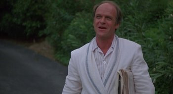 Movie still from “Commando” (1985), directed by Mark L. Lester – A man in a white jacket walking down a street; Medium shot, Low angle