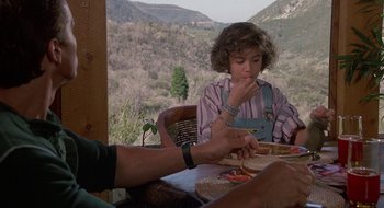 Movie still from “Commando” (1985), directed by Mark L. Lester – A woman sitting at a table eating a sandwich; Medium shot, High angle