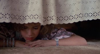 Movie still from “Commando” (1985), directed by Mark L. Lester – A woman laying on the ground under a bed; Close Up shot, High angle