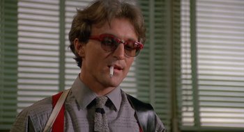 Movie still from “Commando” (1985), directed by Mark L. Lester – A man with a cigarette in his mouth and wearing glasses; Close Up shot, Low angle