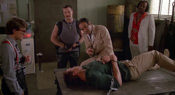 Movie still from “Commando” (1985), directed by Mark L. Lester – A man is tied to the ground by two other men; Medium shot, High angle