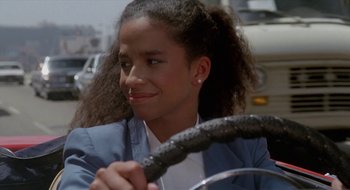 Movie still from “Commando” (1985), directed by Mark L. Lester – A young woman sitting in a car holding a steering wheel; Close Up shot, Low angle