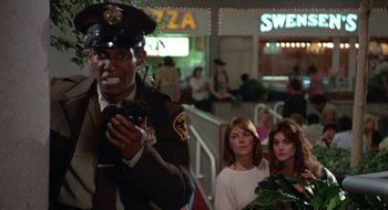 Movie still from “Commando” (1985), directed by Mark L. Lester – A police officer is holding a walkie talkie; Medium shot, Low angle