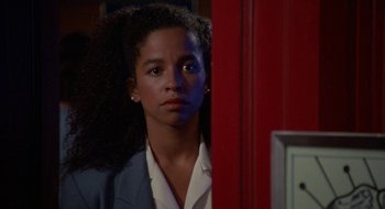 Movie still from “Commando” (1985), directed by Mark L. Lester – A young woman with curly black hair standing in front of a red door; Close Up shot, Over the shoulder angle