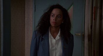 Movie still from “Commando” (1985), directed by Mark L. Lester – A woman in a blue jacket is standing in front of a door; Close Up shot, Over the shoulder angle