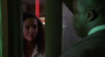 Movie still from “Commando” (1985), directed by Mark L. Lester – A woman standing in front of a wall looking at the camera; Close Up shot, Over the shoulder angle