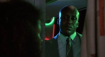 Movie still from “Commando” (1985), directed by Mark L. Lester – A man wearing a suit and tie in front of a neon sign; Close Up shot, Low angle