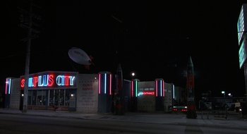 Movie still from “Commando” (1985), directed by Mark L. Lester – A night time view of a gas station and parking lot; Extreme Wide shot, Low angle