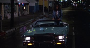 Movie still from “Commando” (1985), directed by Mark L. Lester – A man sitting on the hood of a classic car at night; Wide shot, Low angle