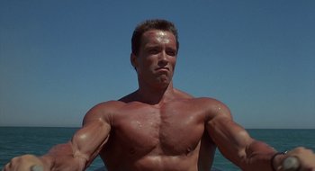 Movie still from “Commando” (1985), directed by Mark L. Lester – A man with no shirt is standing in the water; Medium shot, Low angle
