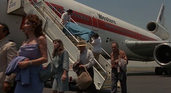 Movie still from “Commando” (1985), directed by Mark L. Lester – A group of people walking up the stairs of an airplane; Wide shot, High angle