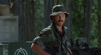 Movie still from “Commando” (1985), directed by Mark L. Lester – A man with a gun in his hand and a hat on; Medium shot, Low angle