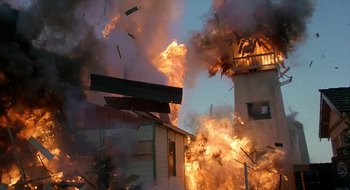 Movie still from “Commando” (1985), directed by Mark L. Lester – A building on fire with smoke coming out of it; Extreme Wide shot, Low angle