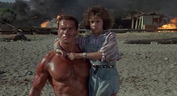 Movie still from “Commando” (1985), directed by Mark L. Lester – A man and a woman standing next to each other on a beach; Medium shot, Low angle