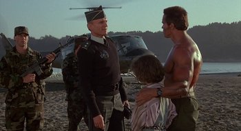 Movie still from “Commando” (1985), directed by Mark L. Lester – A man in a uniform talking to two other men; Medium shot, Over the shoulder angle