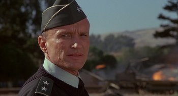 Movie still from “Commando” (1985), directed by Mark L. Lester – A man in a military uniform is looking at the camera; Close Up shot, Low angle