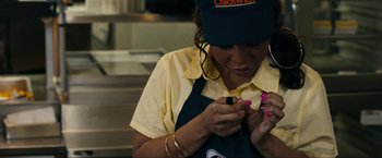 Movie still from “Compliance” (2012), directed by Craig Zobel – A woman in a yellow shirt and a blue hat is looking at her cell phone; Close Up shot, High angle