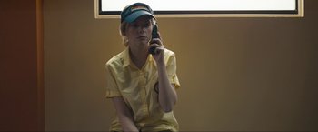 Movie still from “Compliance” (2012), directed by Craig Zobel – A woman in a yellow shirt and a hat is talking on a cell phone; Medium shot, Low angle