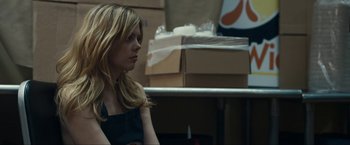 Movie still from “Compliance” (2012), directed by Craig Zobel – A woman sitting in front of a table with boxes in the background; Medium shot, Over the shoulder angle