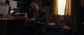 Movie still from “Compliance” (2012), directed by Craig Zobel – A man sitting in a chair writing on a piece of paper; Medium shot, Over the shoulder angle