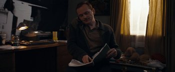 Movie still from “Compliance” (2012), directed by Craig Zobel – A man sitting at a table looking at a book; Medium shot, High angle