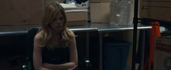 Movie still from “Compliance” (2012), directed by Craig Zobel – A woman sitting on a chair in a dark room; Medium shot, Over the shoulder angle