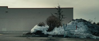 Movie still from “Compliance” (2012), directed by Craig Zobel – A shopping cart sitting next to a pile of snow next to a building; Extreme Wide shot, Low angle