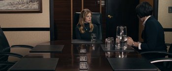 Movie still from “Compliance” (2012), directed by Craig Zobel – A woman sitting at a conference table with a glass of water; Medium shot, Over the shoulder angle