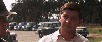 Movie still from “Cool Hand Luke” (1967), directed by Stuart Rosenberg – A person wearing a white shirt near some cars; Close Up shot, Over the shoulder angle