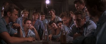 Movie still from “Cool Hand Luke” (1967), directed by Stuart Rosenberg – A group of men sitting at a table with bottles; Medium shot, High angle