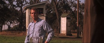 Movie still from “Cool Hand Luke” (1967), directed by Stuart Rosenberg – A man standing in front of an outhouse in a field; Medium shot, Low angle