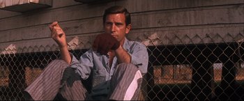 Movie still from “Cool Hand Luke” (1967), directed by Stuart Rosenberg – A man sitting on the ground with his hand in his mouth; Close Up shot, Low angle