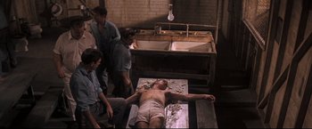 Movie still from “Cool Hand Luke” (1967), directed by Stuart Rosenberg – A group of people standing around a man laying on a bed; Wide shot, High angle