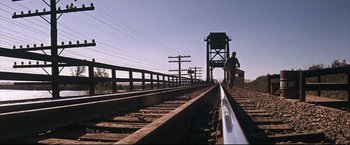 Movie still from “Cool Hand Luke” (1967), directed by Stuart Rosenberg – A man standing on a train track near a bridge; Wide shot, Low angle