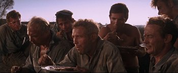 Movie still from “Cool Hand Luke” (1967), directed by Stuart Rosenberg – A group of men sitting next to each other eating food; Medium shot, Low angle