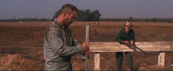 Movie still from “Cool Hand Luke” (1967), directed by Stuart Rosenberg – A man in a field holding a metal pole; Medium shot, Low angle
