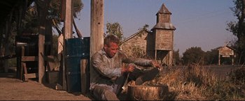 Movie still from “Cool Hand Luke” (1967), directed by Stuart Rosenberg – A man sitting on the ground near a tree stump; Wide shot, Low angle