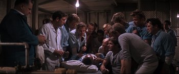 Movie still from “Cool Hand Luke” (1967), directed by Stuart Rosenberg – A group of men standing around a man lying on a table; Medium shot, High angle