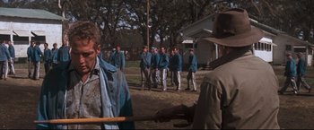 Movie still from “Cool Hand Luke” (1967), directed by Stuart Rosenberg – A group of men standing in a field with a stick; Medium shot, Over the shoulder angle