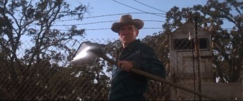 Movie still from “Cool Hand Luke” (1967), directed by Stuart Rosenberg – An older man holding a shovel near a barbed - wire fence; Medium shot, Low angle