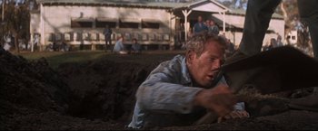 Movie still from “Cool Hand Luke” (1967), directed by Stuart Rosenberg – A man is digging in the dirt while people watch; Medium shot, High angle