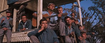 Movie still from “Cool Hand Luke” (1967), directed by Stuart Rosenberg – A group of men sitting next to each other on a porch; Medium shot, Low angle