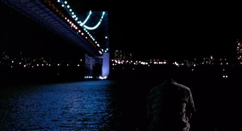 Movie still from “Cop Land” (1997), directed by James Mangold – A man standing in front of a body of water at night; Extreme Wide shot, Over the shoulder angle