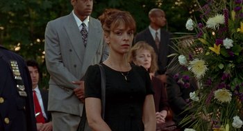 Movie still from “Cop Land” (1997), directed by James Mangold – A woman in a black dress standing in front of a group of people; Medium shot, Over the shoulder angle