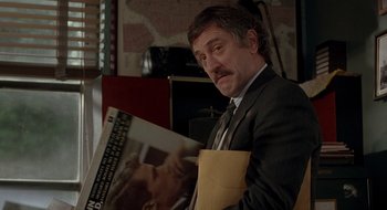 Movie still from “Cop Land” (1997), directed by James Mangold – A man in a suit and tie holding a magazine; Close Up shot, Over the shoulder angle